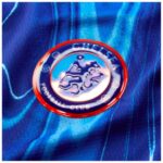 Chelsea FC crest on blue fabric, featuring the lion emblem and red circular border as part of a club badge on a shirt