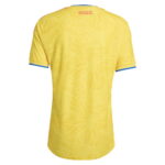 Back view of a yellow Colombia national team soccer jersey with blue trim on sleeves and a subtle tie-dye pattern; COLOMBIA text near the collar.