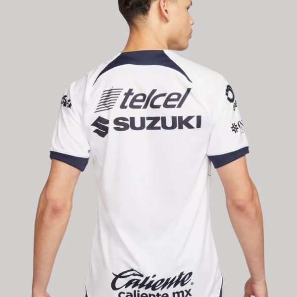 Back view of a man wearing a white sports jersey with Telcel and Suzuki logos and Caliente.mx at the hem, navy trim on sleeves and collar.