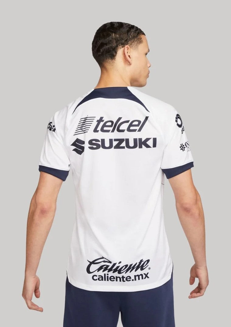rhaBkMnjZDf2NnQ_ba270924-8f7b-4f4e-b7ad-7172c6da5a29 | UAE SPORT STORE Back view of a man wearing a white sports jersey with Telcel and Suzuki logos and Caliente.mx at the hem, navy trim on sleeves and collar.