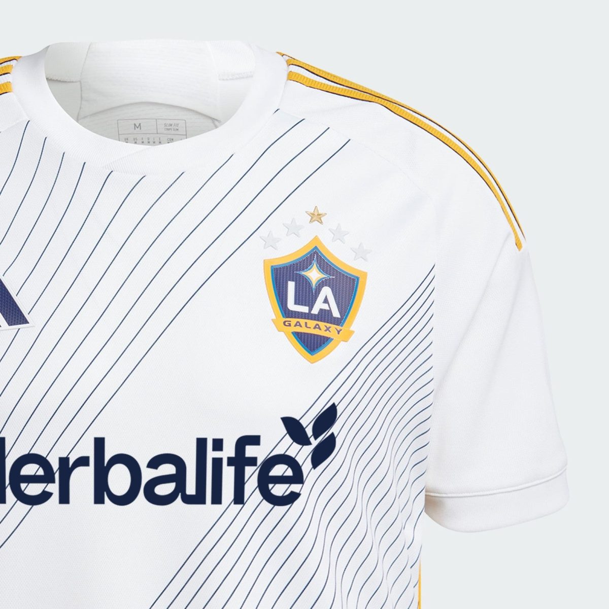White LA Galaxy soccer jersey close-up with pinstripes, team crest, and Herbalife sponsor text visible, yellow shoulder trim.
