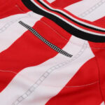 Close-up of a red-and-white striped sports jersey with a black-and-white zipper graphic and visible stitching.