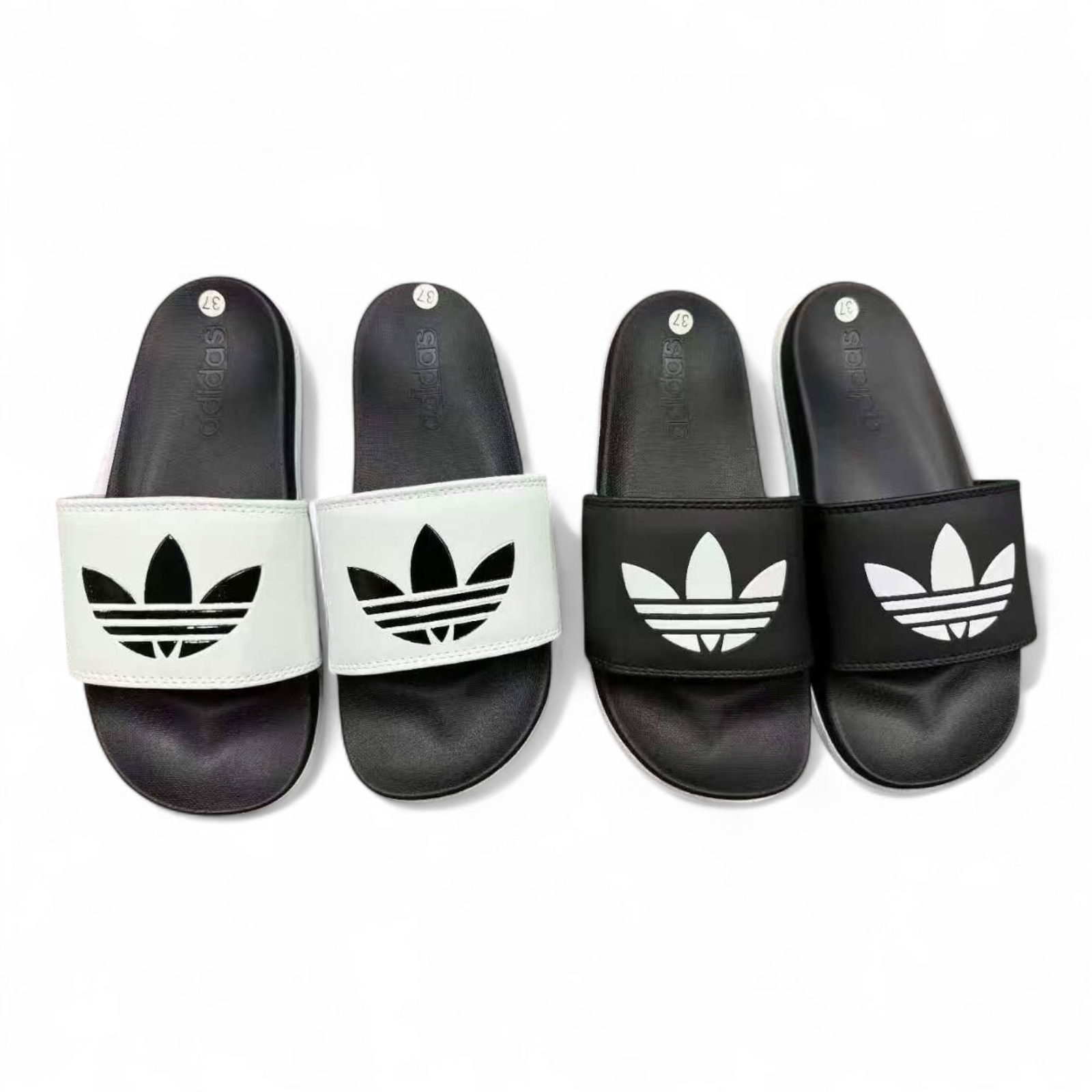 rn-image_picker_lib_temp_01e54532-04f5-4f66-8392-726c9cfa83e8 Four Adidas slide sandals arranged in a row: two white-strapped sandals on the left and two black-strapped sandals on the right, all with a prominent trefoil logo on the strap.