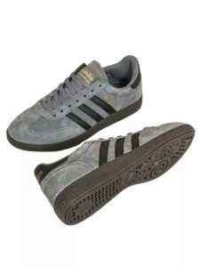 Pair of gray suede Adidas sneakers with black three-stripe branding, shown from side and bottom to display sole details.