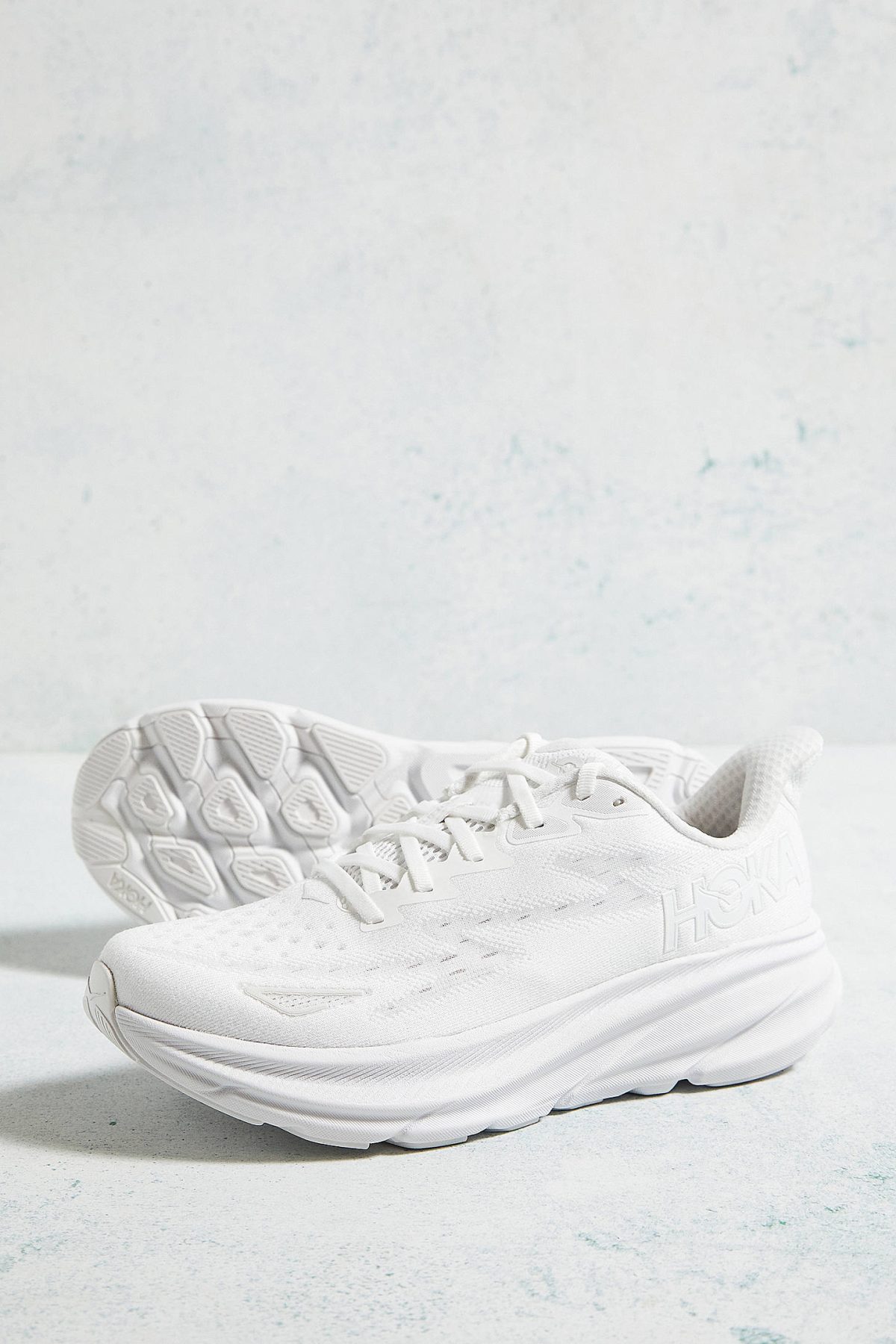 White athletic sneakers with textured soles resting on a pale blue surface.