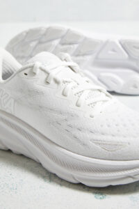 Close-up of white running shoes with laces, knit texture, and a thick sole on a light speckled surface.
