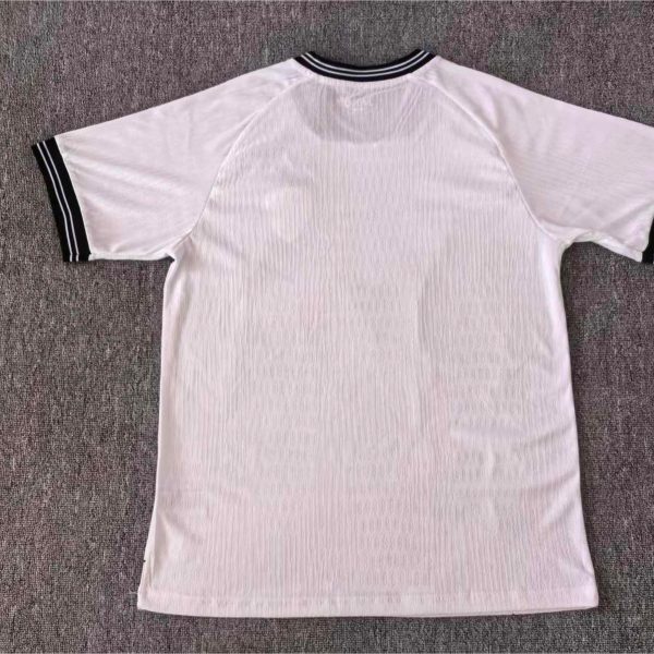 White short-sleeve polo shirt with black striped collar and cuffs laid flat on a gray carpeted surface.