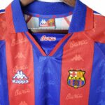 rn-image_picker_lib_temp_05cec11d-5822-4eb4-8294-b1d0eba1487c | UAE SPORT STORE Close-up of a FC Barcelona jersey neckline: blue and red vertical stripes, Kappa logos, and the Barça crest visible on the chest area.