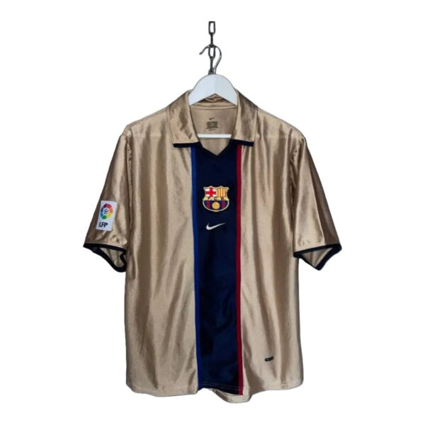 Beige FC Barcelona soccer jersey on a hanger with a dark blue center panel, red stripe, and team crest on the chest