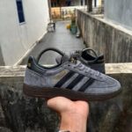 Grey Adidas sneakers with black stripes held in a hand outdoors, showing the side label reading 'SPECIAL' and a brown sole.