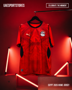 Egypt 2026 home jersey on a hanger, red geometric design with Puma logo and team crest, displayed in a neon-lit setting with the caption 'EGYPT 2026 HOME JERSEY'.
