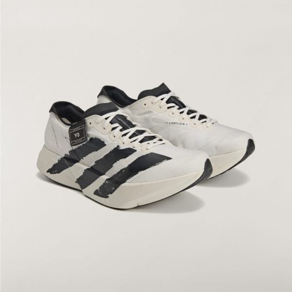 White and black athletic sneakers with three bold black stripes on the sides, placed on a light background, cropped bottom portion visible.