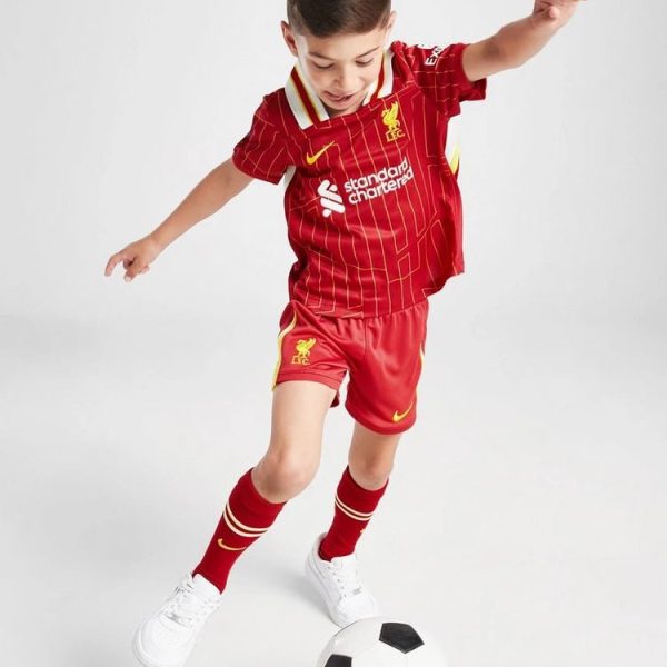 Young boy in a red Liverpool FC jersey kicks a soccer ball on a white background.