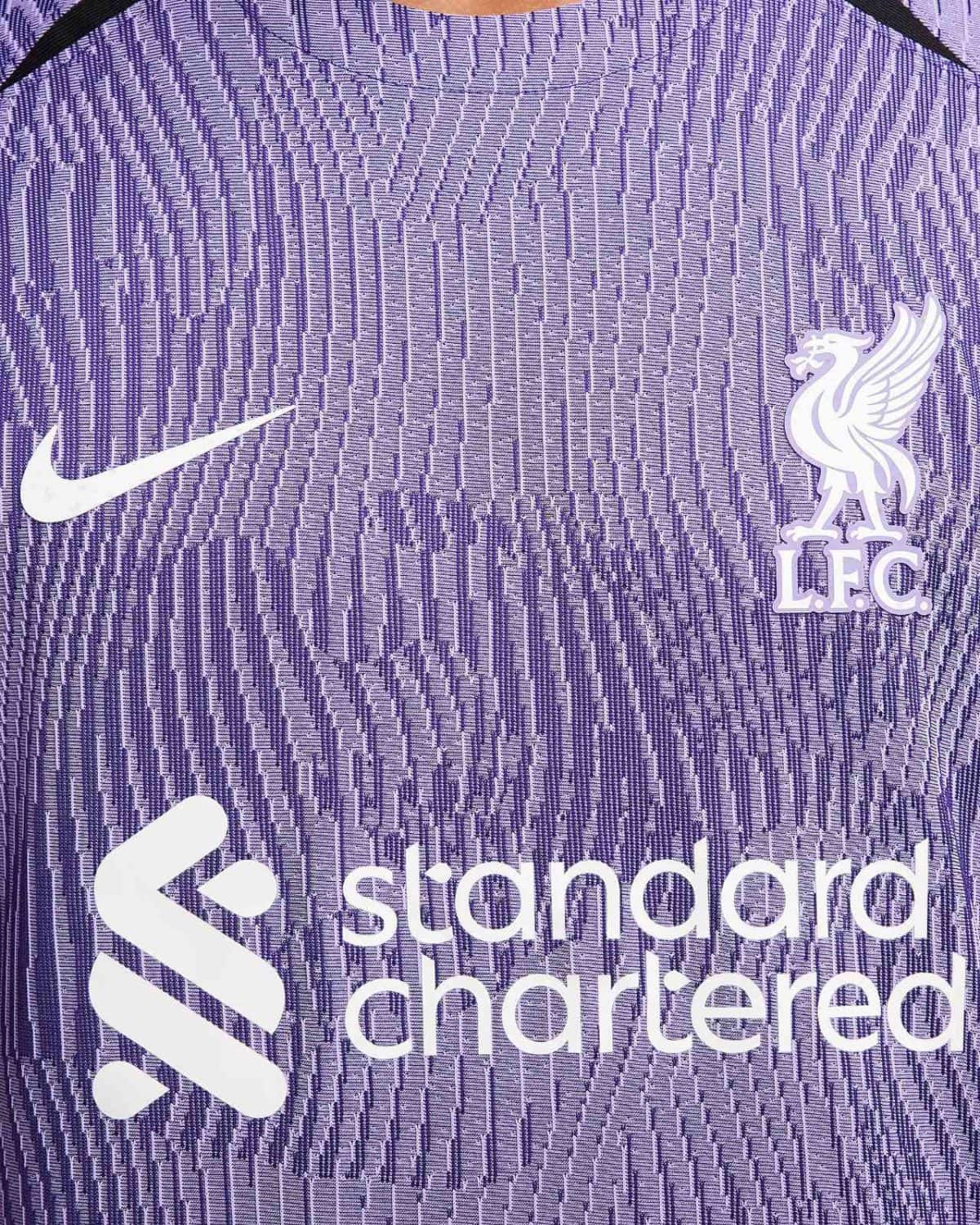 Close-up of a purple Liverpool FC jersey featuring the white Nike swoosh and the club crest with sponsor text nearby.