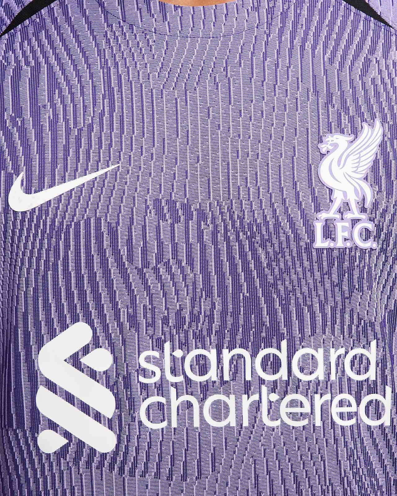 rn-image_picker_lib_temp_0c24d7af-4250-431b-9757-f13a50c77087 | UAE SPORT STORE Close-up of a purple Liverpool FC jersey featuring the white Nike swoosh and the club crest with sponsor text nearby.