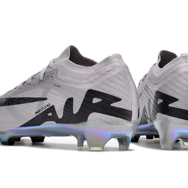 Pair of light gray soccer cleats with black accents and iridescent sole plates on a white background.