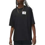 Person wearing a black oversized T-shirt with a white square patch featuring a Jumpman logo on the chest, model with braided hair left visible.