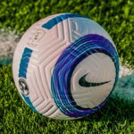 White Nike soccer ball with blue and purple circular design resting on green grass.