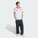 Male model in a white UAE FA jersey with red trim, standing against a light gray background with hands in pockets.
