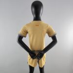 Back view of a black mannequin wearing a tan short-sleeve shirt with striped sleeve cuffs and UNHCR logo on the lower back, arms crossed behind the torso.