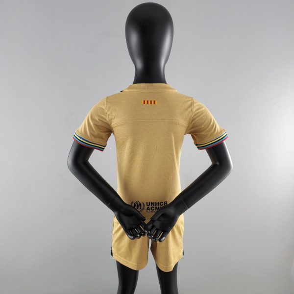 Back view of a black mannequin wearing a tan short-sleeve shirt with striped sleeve cuffs and UNHCR logo on the lower back, arms crossed behind the torso.