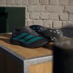 Grey athletic shoes with teal stripes resting on a wooden bench against a brick wall behind them.