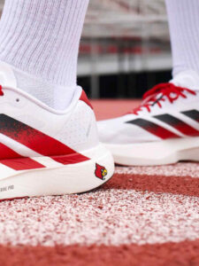 rn-image_picker_lib_temp_198ccc97-7255-43d5-a510-616623c6c697 | UAE SPORT STORE Close-up of white and red running shoes with a Cardinal logo on the heel, standing on a red track surface