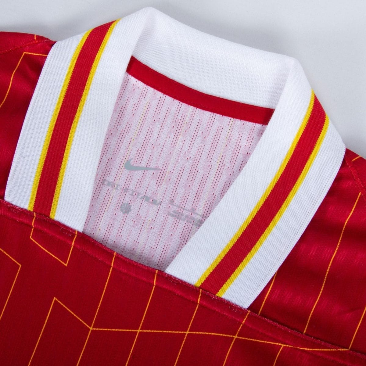 Close-up of a red athletic jersey with a white collar trimmed in red and yellow stripes, showing mesh fabric inside.
