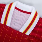 Close-up of a red athletic jersey with a white collar trimmed in red and yellow stripes, showing mesh fabric inside.