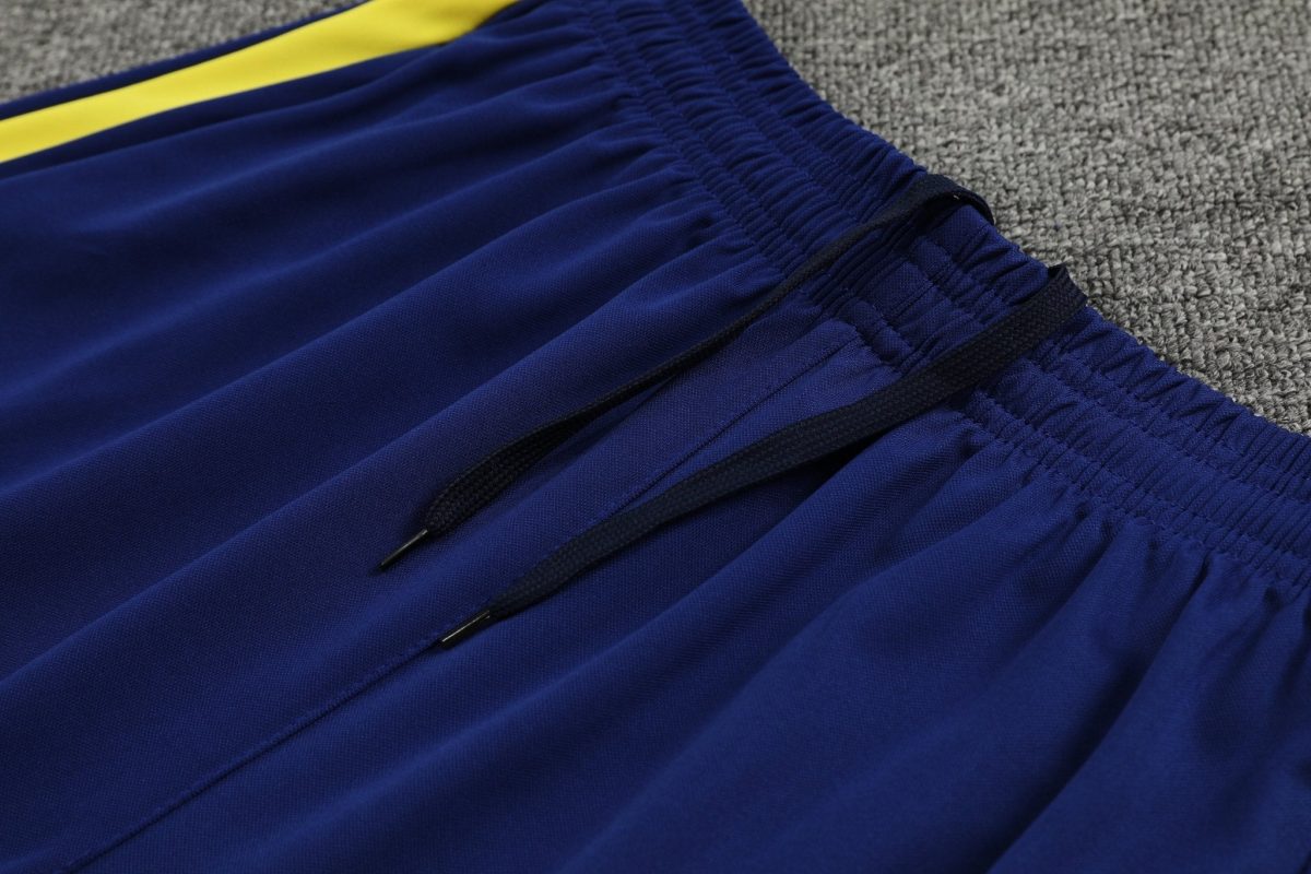 Close-up of blue athletic pants with a yellow stripe and smocked waistband with drawstrings on a gray carpeted surface.