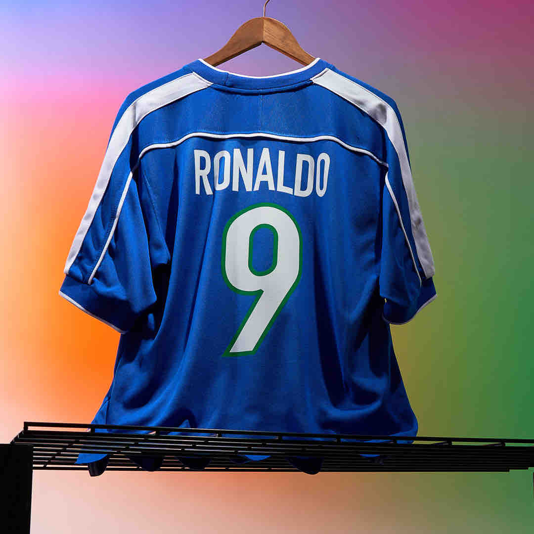 rn-image_picker_lib_temp_28d14b3a-351d-4832-afee-236d64e49d75 | UAE SPORT STORE Blue Ronaldo soccer jersey with the number 9 hanging on a hanger against a colorful gradient background.