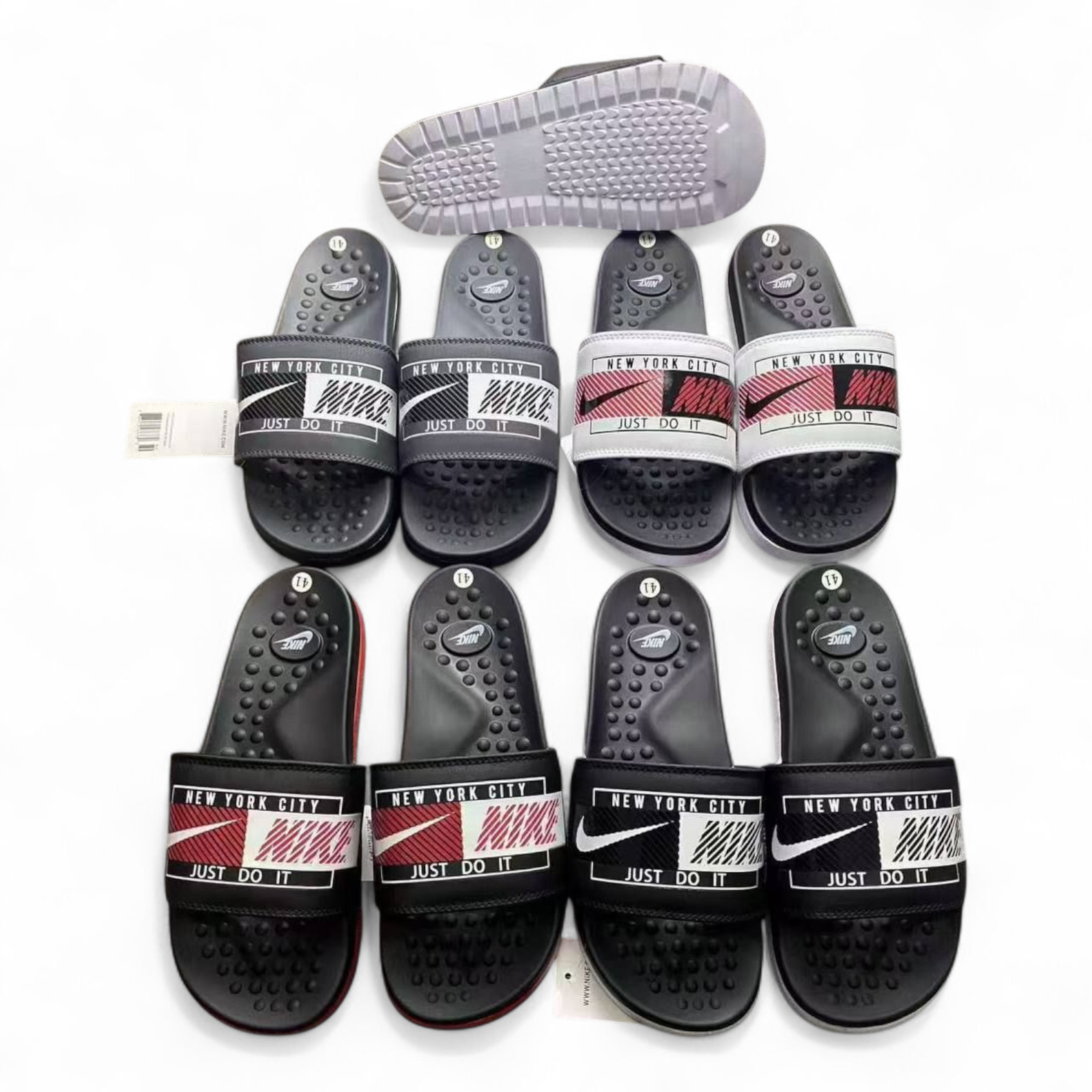 rn-image_picker_lib_temp_29014ec2-e578-4096-91c7-276365728320 Row of black Nike slide sandals with 'New York City' and 'Just Do It' straps on a white background.
