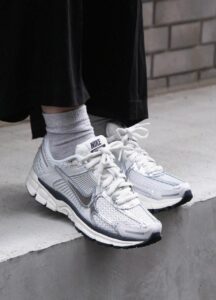 White Nike running shoes with silver accents on concrete steps, gray socks visible above the shoes.