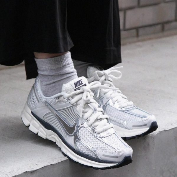 White Nike running shoes with silver accents on concrete steps, gray socks visible above the shoes.