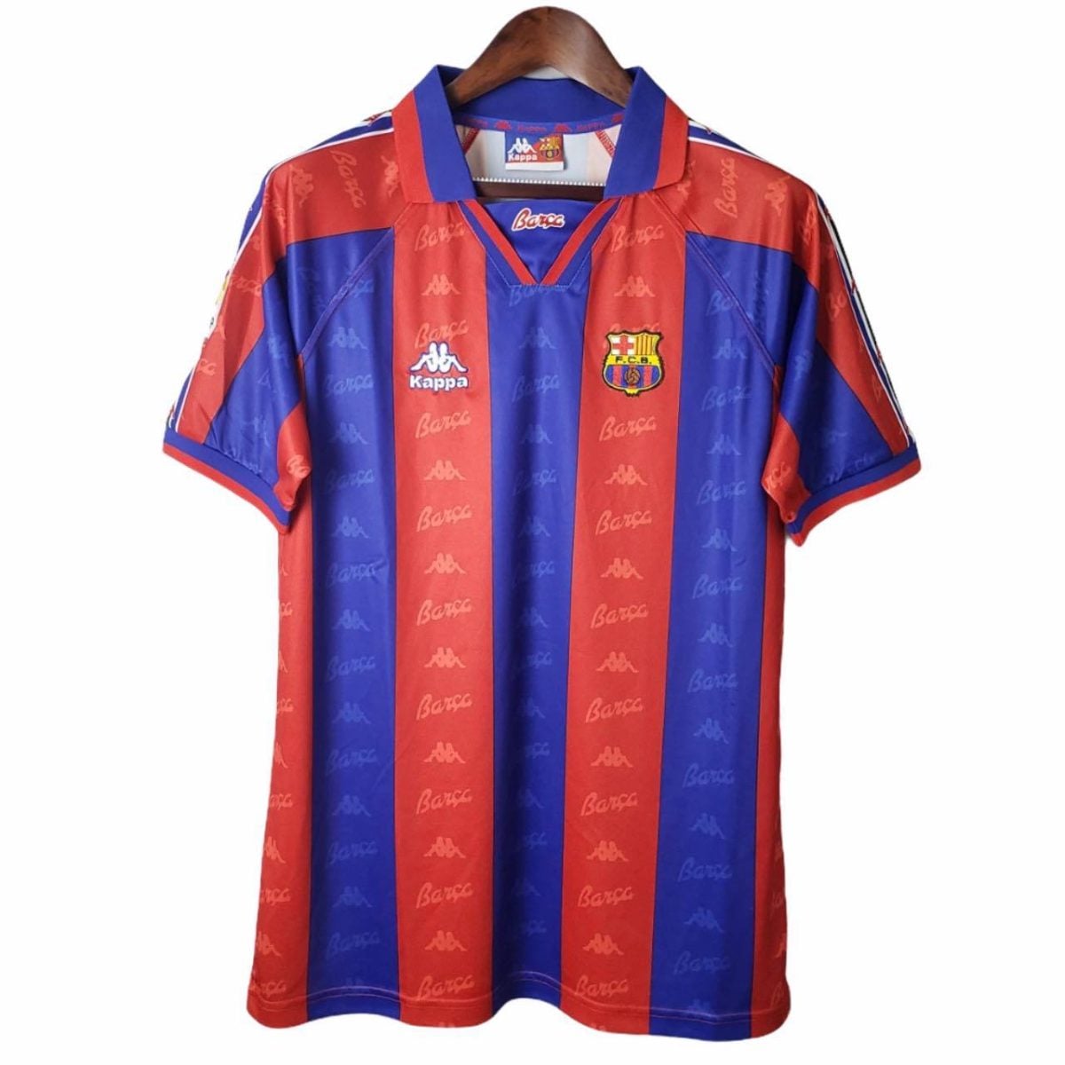 Red and blue striped FC Barcelona soccer jersey with crest, hanging on a wooden hanger.