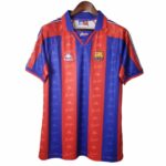 rn-image_picker_lib_temp_2c0f4d50-5ecd-40d8-8104-d4cc15ab5bad | UAE SPORT STORE Red and blue striped FC Barcelona soccer jersey with crest, hanging on a wooden hanger.