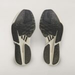 Two white athletic shoes viewed from the bottom, showing black textured outsoles side by side.