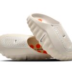 Cream-colored slip-on athletic shoes with perforated upper and wavy sole, Nike logo visible on side.