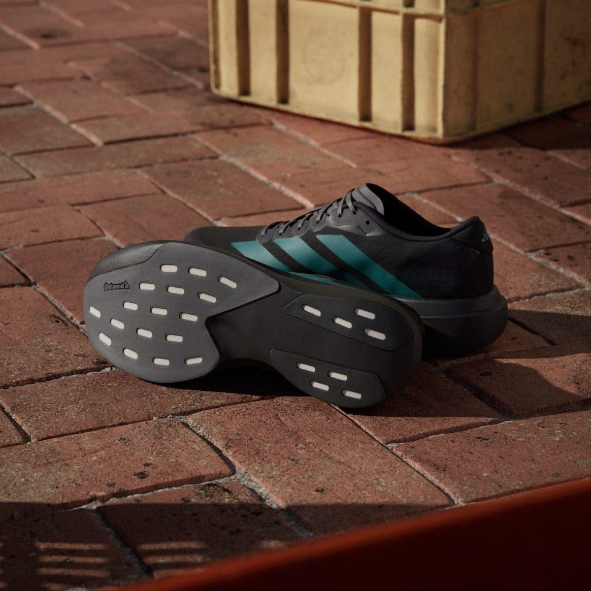 Pair of dark gray running shoes with teal stripes resting on a brick patio