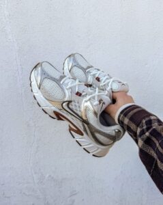 rn-image_picker_lib_temp_3787154d-3e34-4b1c-9947-78e9e93a4a06 | UAE SPORT STORE A person holding a pair of white and silver running shoes against a light wall backdrop.
