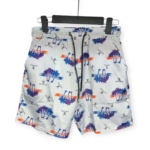 White Louis Vuitton swim shorts with blue, purple, and orange palm tree print, hanging on a black hanger