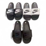 Display of four Nike slide sandals in black, white, and gray arranged in a row, showing Nike swoosh logos on the straps