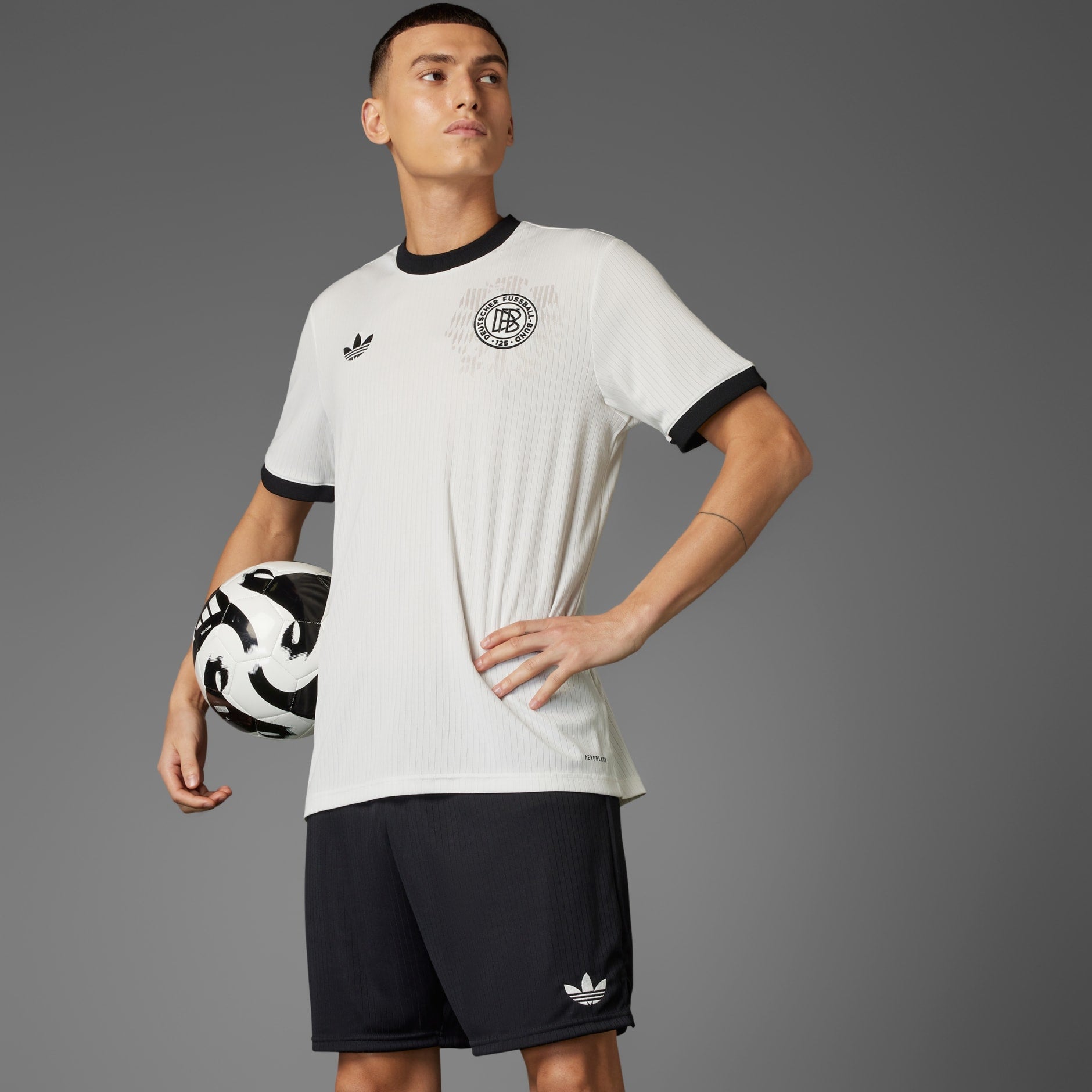 rn-image_picker_lib_temp_3d50a883-16c2-40c9-8c49-2d44526dc3c4 | UAE SPORT STORE Athlete in a white soccer jersey holding a black-and-white soccer ball against a gray backdrop.