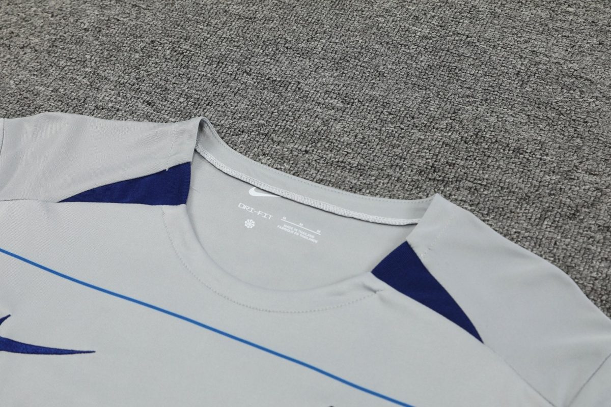 Close-up of a light gray athletic shirt with blue accents, showing the Nike swoosh and Dri-FIT branding on a carpeted background.