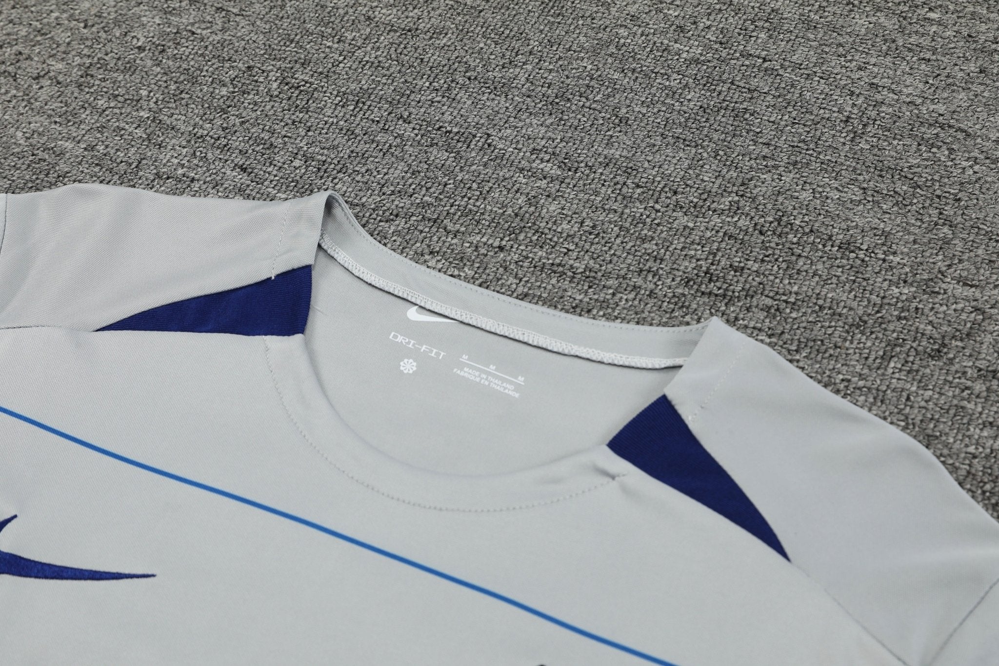 rn-image_picker_lib_temp_45a898ab-86eb-4dc7-9db1-190497ed6268 | UAE SPORT STORE Close-up of a light gray athletic shirt with blue accents, showing the Nike swoosh and Dri-FIT branding on a carpeted background.