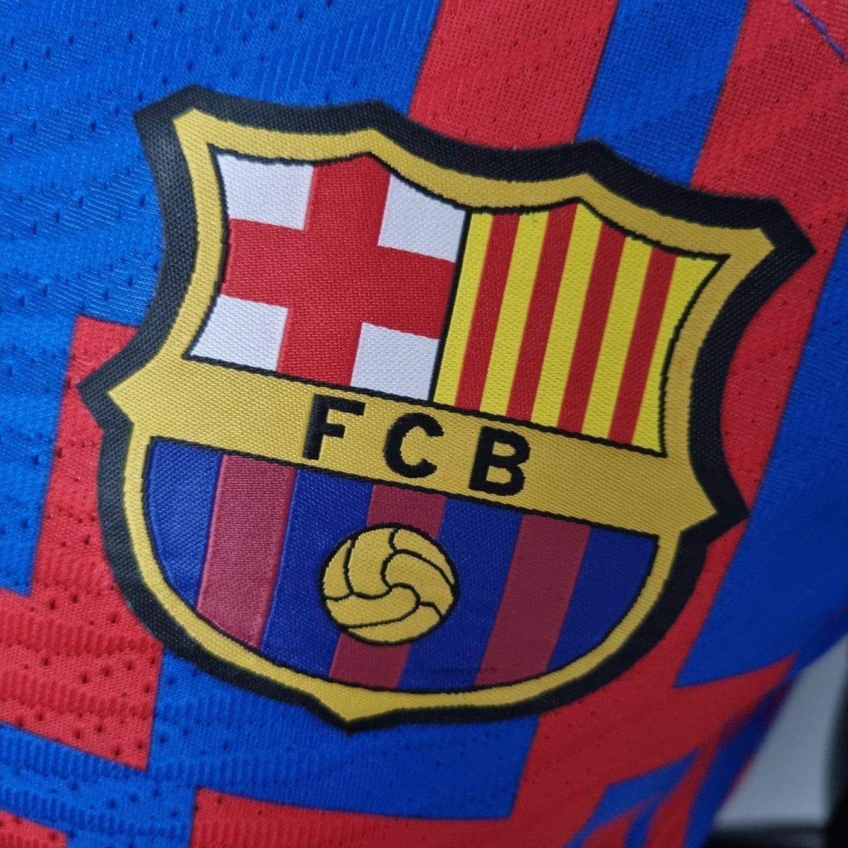 Close-up of a yellow shield crest on a red-and-blue striped fabric, resembling a sports team emblem (FCBarcelona).