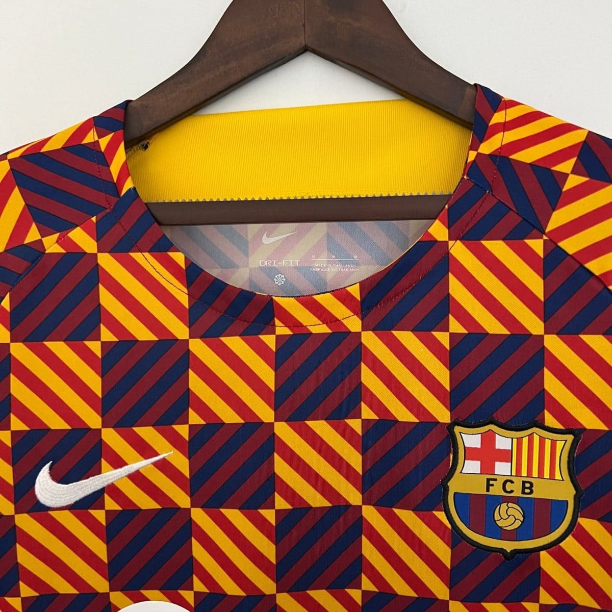 Close-up of a colorful geometric-patterned jacket (red, yellow, blue) on a hanger, showing a yellow collar lining and partial logos (Nike swoosh and FC Barcelona crest).