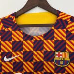 Close-up of a colorful geometric-patterned jacket (red, yellow, blue) on a hanger, showing a yellow collar lining and partial logos (Nike swoosh and FC Barcelona crest).
