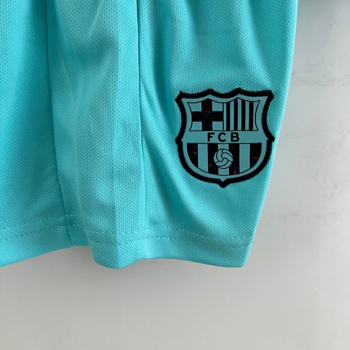 Close-up of a turquoise mesh sports jersey with a partial FC Barcelona crest visible on the right side.