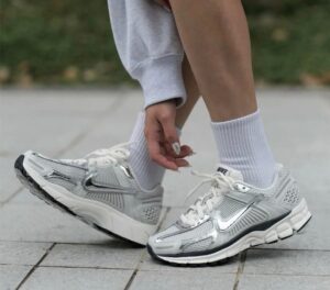 Person ties white laces on silver Nike running shoes on a gray sidewalk